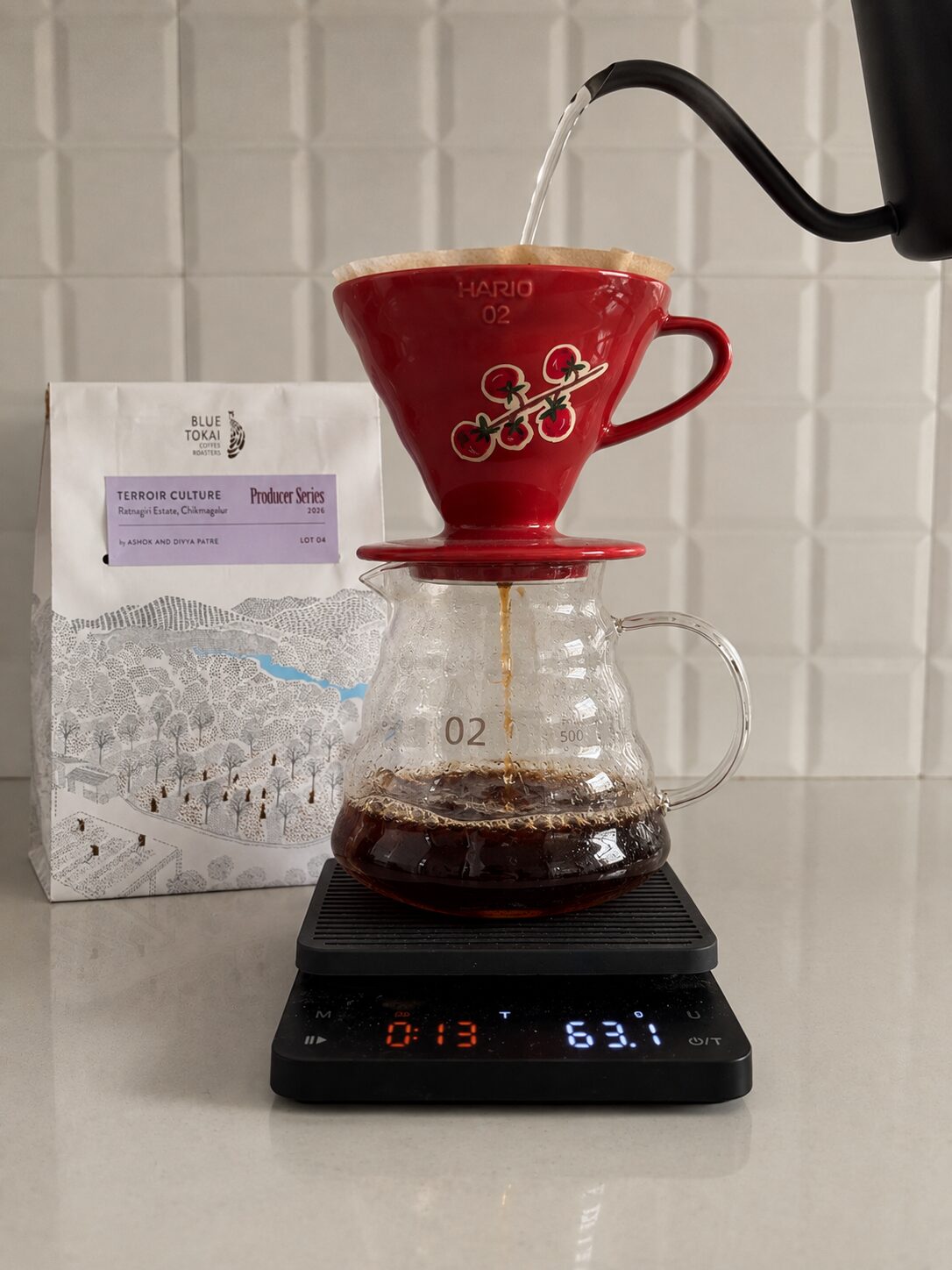 A red Hario V60 dripper over a glass carafe on a scale, next to a Blue Tokai Terroir Culture bag from Ratnagiri Estate.